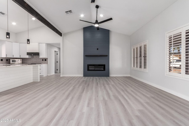 unfurnished living room featuring ceiling fan, lofted ceiling with beams, a large fireplace, and light hardwood / wood-style flooring