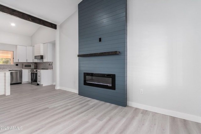 unfurnished living room with lofted ceiling with beams, a large fireplace, and light hardwood / wood-style flooring