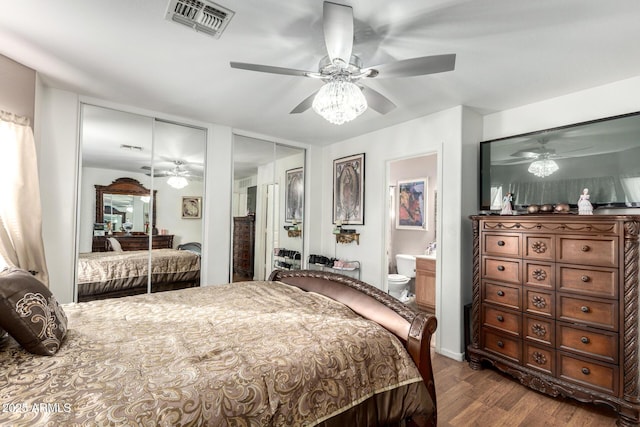 bedroom featuring dark wood-type flooring, ensuite bathroom, ceiling fan, and multiple closets