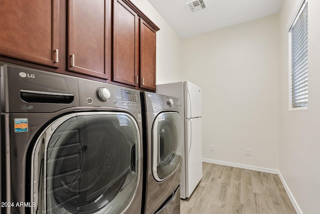 clothes washing area featuring washer and clothes dryer, cabinets, and light hardwood / wood-style flooring