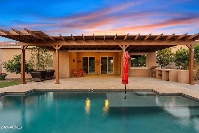 pool at dusk with grilling area, a patio area, and exterior kitchen