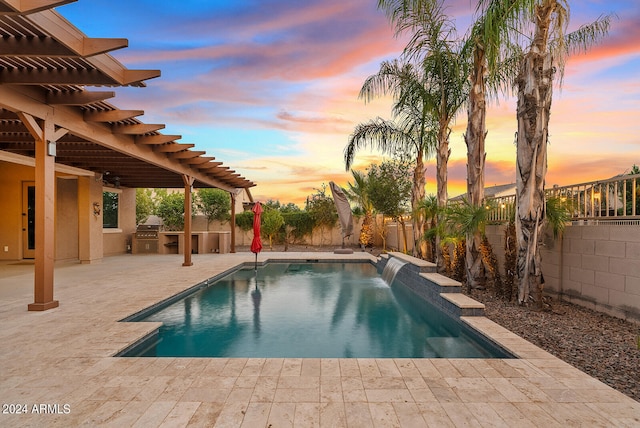 pool at dusk with an outdoor kitchen, a patio area, a pergola, and pool water feature