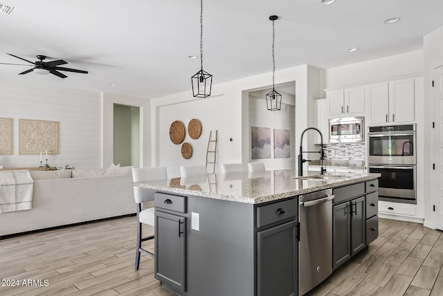 kitchen featuring a kitchen island with sink, sink, white cabinetry, appliances with stainless steel finishes, and a kitchen bar