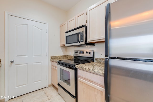 kitchen featuring light brown cabinets, stainless steel appliances, light stone counters, and light tile patterned floors