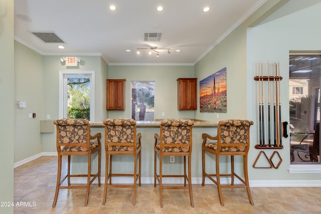 kitchen featuring light stone counters, kitchen peninsula, ornamental molding, and a kitchen bar