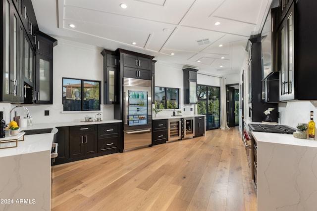 kitchen with light stone counters, light hardwood / wood-style flooring, beverage cooler, sink, and high quality appliances