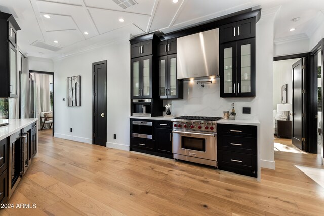 kitchen with coffered ceiling, wall chimney exhaust hood, ornamental molding, light wood-type flooring, and appliances with stainless steel finishes