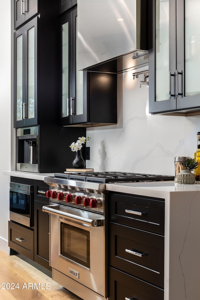 kitchen with light stone countertops, wall chimney exhaust hood, light hardwood / wood-style flooring, and designer stove