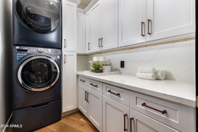 clothes washing area with stacked washer and clothes dryer, cabinets, and light hardwood / wood-style flooring