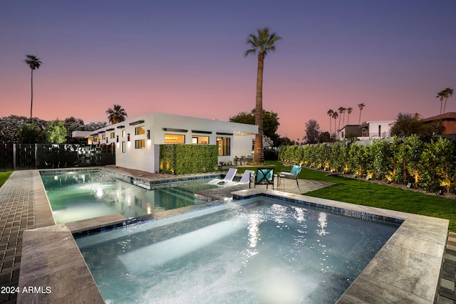 pool at dusk featuring an in ground hot tub and a lawn