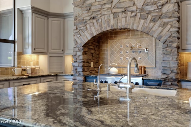 kitchen with sink, gray cabinets, dark stone countertops, and backsplash