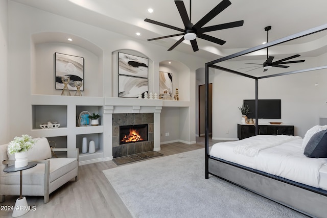 bedroom featuring light hardwood / wood-style floors, ceiling fan, and a tiled fireplace