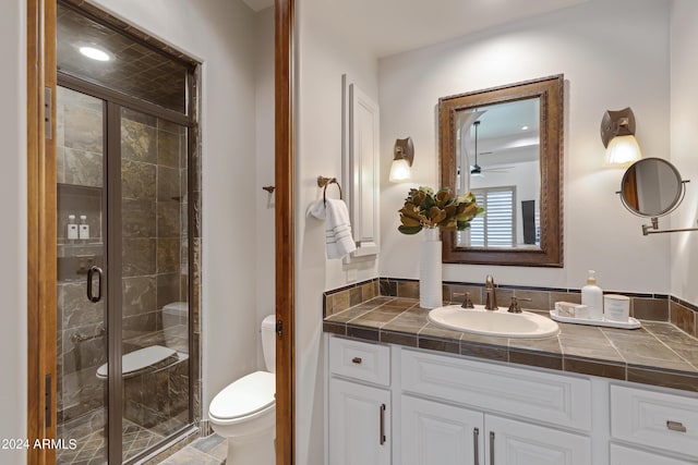 bathroom with ceiling fan, vanity, a shower with shower door, and toilet