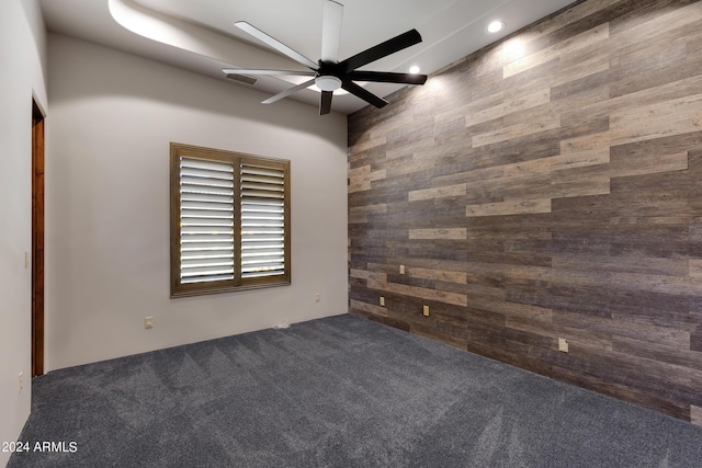 carpeted empty room featuring wooden walls and ceiling fan