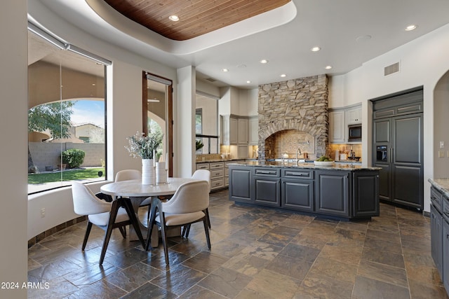 kitchen with light stone countertops, built in appliances, a center island with sink, and gray cabinetry