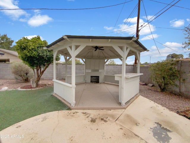 view of patio with a gazebo, a ceiling fan, a fenced backyard, and an outdoor fireplace