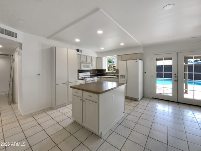 kitchen with a sink, a kitchen island, french doors, white appliances, and light tile patterned floors