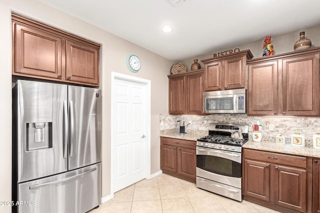 kitchen with light stone counters, decorative backsplash, brown cabinets, light tile patterned floors, and stainless steel appliances