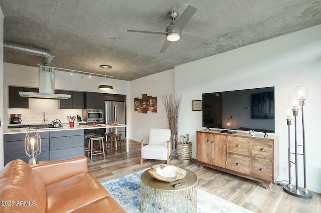 living room featuring a ceiling fan, rail lighting, light wood-style flooring, and baseboards