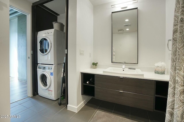 laundry area featuring laundry area, dark tile patterned floors, a sink, visible vents, and stacked washer and clothes dryer