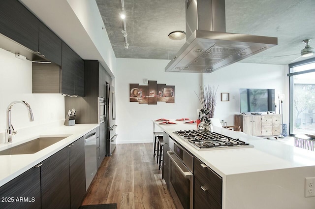 kitchen with island range hood, dark wood-type flooring, a sink, appliances with stainless steel finishes, and track lighting