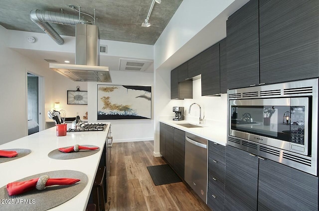 kitchen featuring island range hood, appliances with stainless steel finishes, dark wood-type flooring, light countertops, and a sink