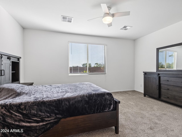 carpeted bedroom with a barn door and ceiling fan