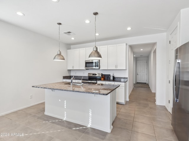 kitchen featuring appliances with stainless steel finishes, hanging light fixtures, white cabinets, dark stone countertops, and a kitchen island with sink