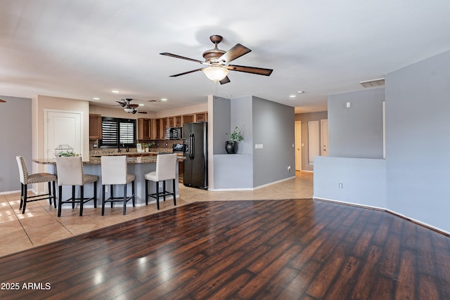 kitchen with decorative backsplash, light wood-type flooring, a breakfast bar area, and black appliances