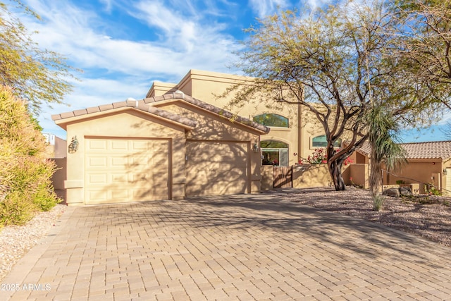 mediterranean / spanish home with decorative driveway, an attached garage, a tile roof, and stucco siding