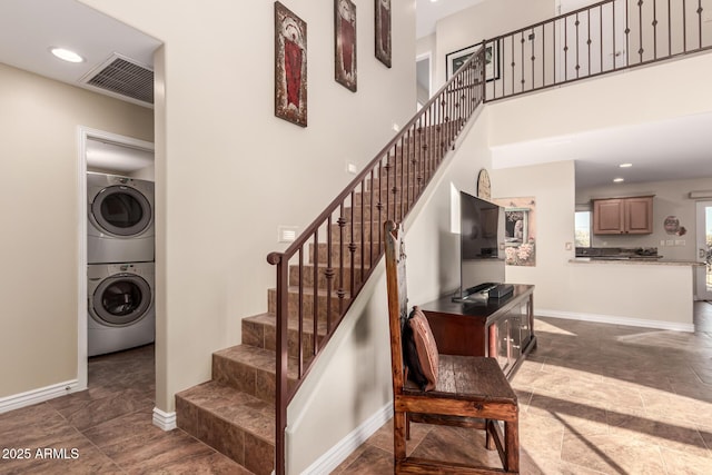 stairs featuring baseboards, visible vents, a towering ceiling, stacked washing maching and dryer, and recessed lighting