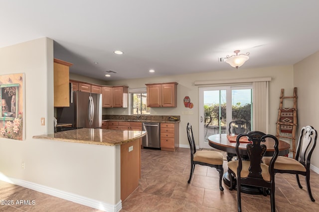 kitchen featuring a peninsula, light stone countertops, baseboards, and stainless steel appliances