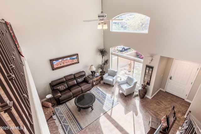 living area with ceiling fan, a high ceiling, and baseboards