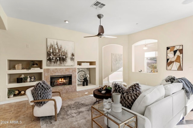 living room featuring built in shelves, ceiling fan, and a tiled fireplace