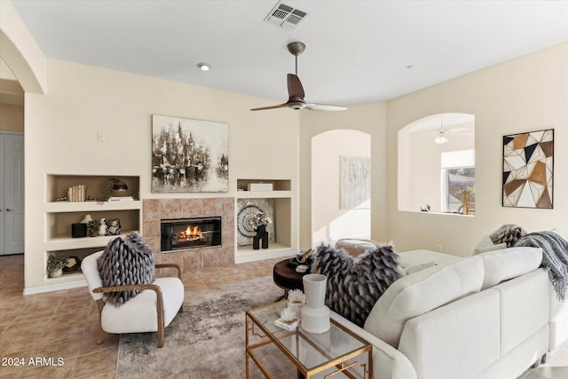 living room with a tile fireplace, built in features, and ceiling fan