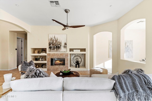 living room with built in shelves, ceiling fan, and a tiled fireplace