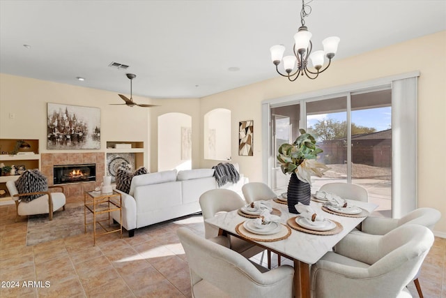 dining area featuring a tile fireplace, light tile patterned floors, and ceiling fan with notable chandelier