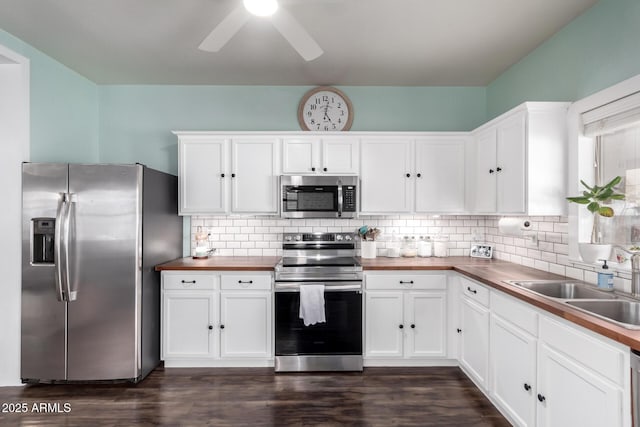 kitchen featuring appliances with stainless steel finishes, butcher block countertops, a sink, and white cabinetry