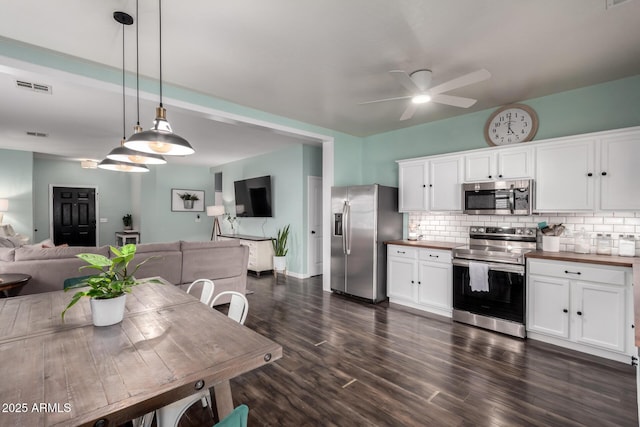 kitchen with tasteful backsplash, white cabinets, butcher block countertops, open floor plan, and stainless steel appliances