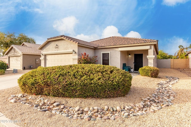 mediterranean / spanish-style house featuring a tile roof, stucco siding, fence, a garage, and driveway