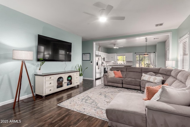 living area with dark wood-type flooring, visible vents, ceiling fan, and baseboards