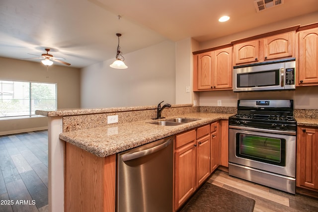 kitchen with pendant lighting, sink, kitchen peninsula, stainless steel appliances, and light stone countertops