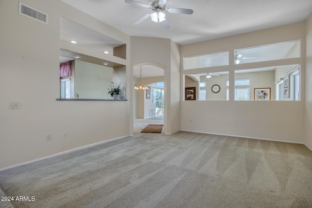 carpeted spare room featuring a towering ceiling and ceiling fan with notable chandelier