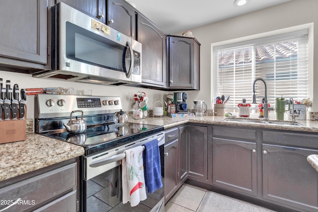 kitchen with sink, light stone countertops, appliances with stainless steel finishes, dark brown cabinets, and light tile patterned flooring