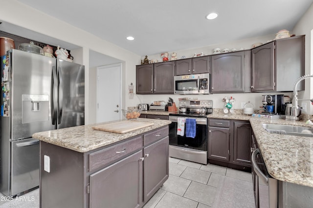 kitchen with dark brown cabinetry, stainless steel appliances, sink, light tile patterned floors, and a kitchen island