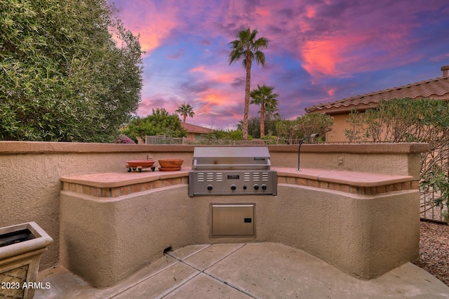 patio terrace at dusk featuring area for grilling and an outdoor kitchen