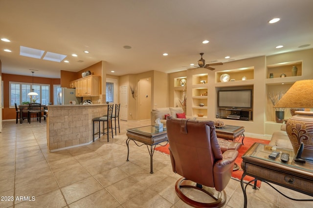 living room featuring built in features, a skylight, ceiling fan, and light tile floors