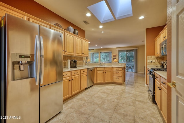 kitchen featuring tasteful backsplash, a skylight, stainless steel appliances, kitchen peninsula, and light tile flooring