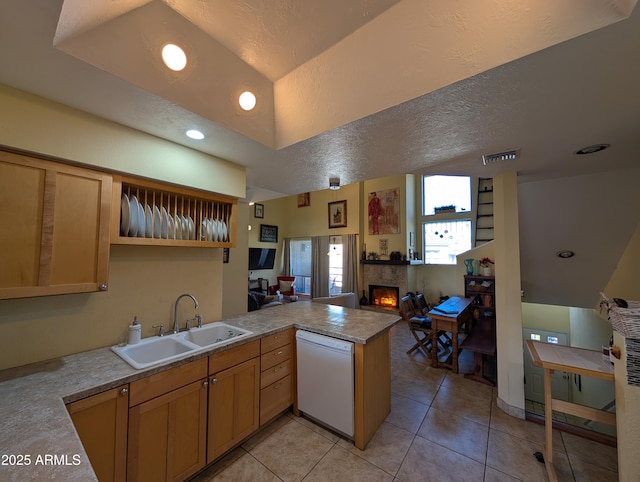 kitchen featuring sink, light tile patterned floors, a tile fireplace, dishwasher, and kitchen peninsula