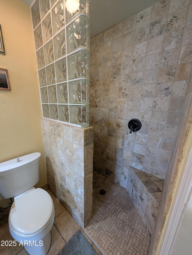 bathroom featuring tiled shower, toilet, and tile patterned flooring